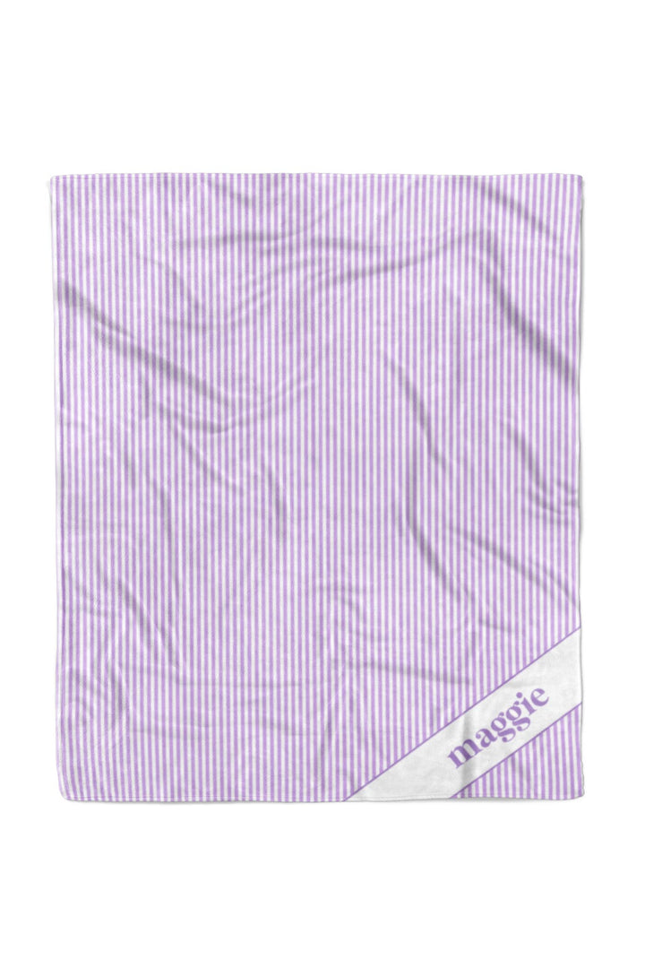 Personalized pet blanket in lavender and white vertical stripes with the name maggie embroidered in purple script on a white satin corner patch