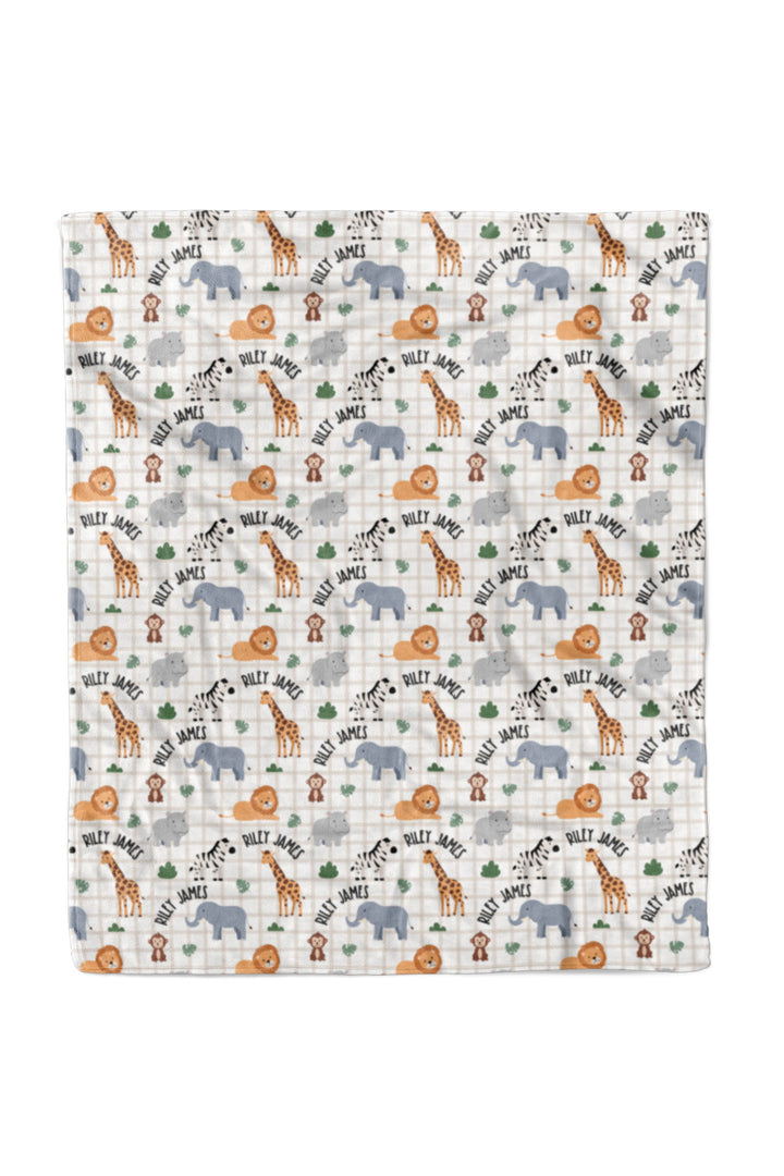 Flat lay of a Caden Lane personalized 50x60 plush blanket in a Wild Child print featuring safari animals on cream plaid, with arched name text reading "Riley James."