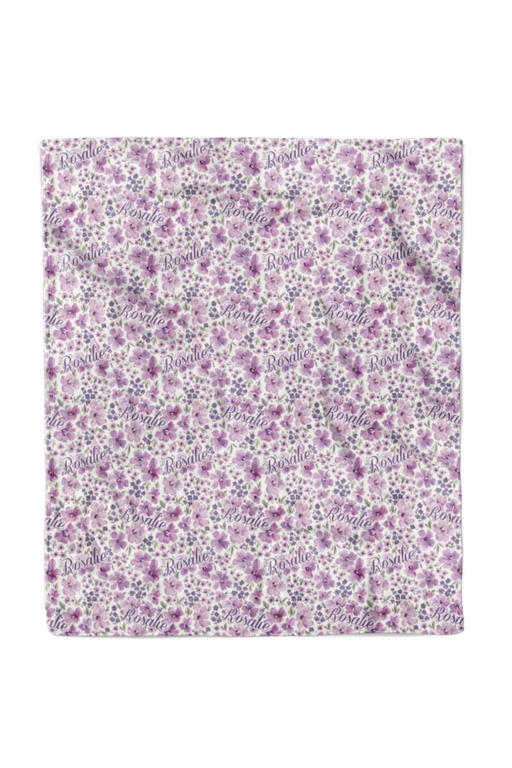 Flat lay of a fully spread Caden Lane white plush 50x60 blanket in a Lilac Dreams print featuring purple and pink watercolor flowers, reading "Rosalie."