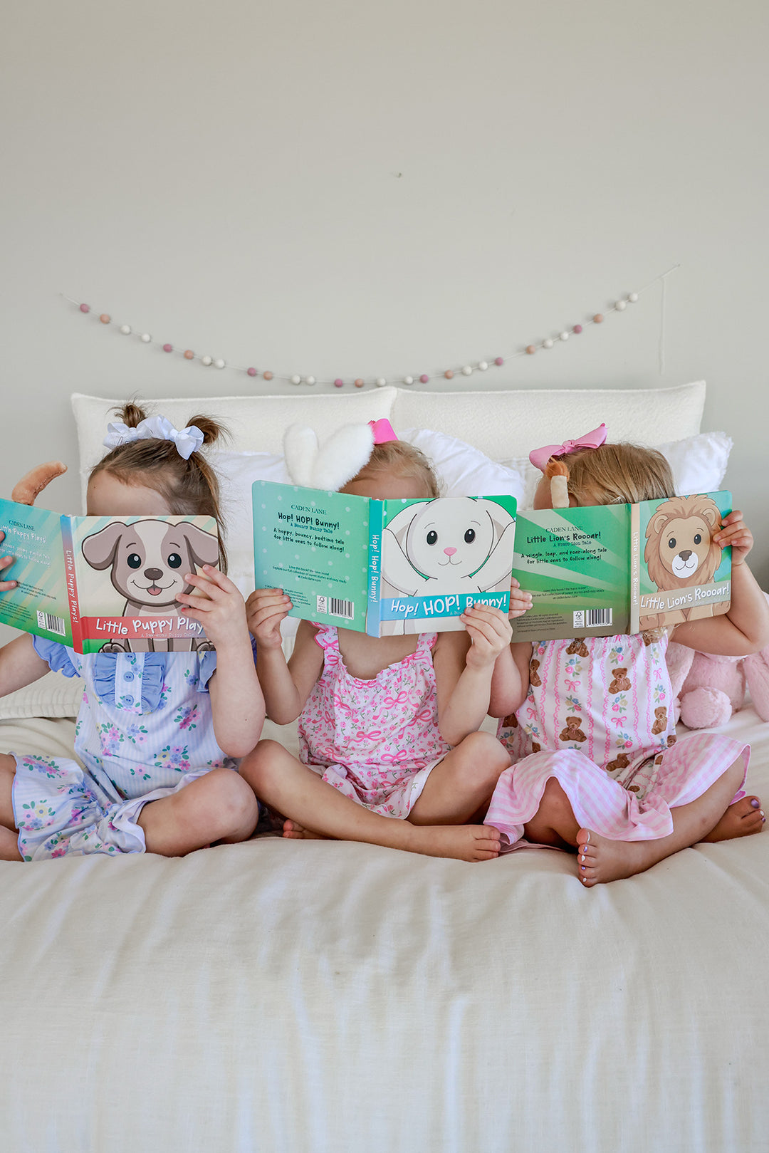Three young girls sitting on a bed each reading a different Cuddle Plush Friends Story Book, front showing Parker Puppy