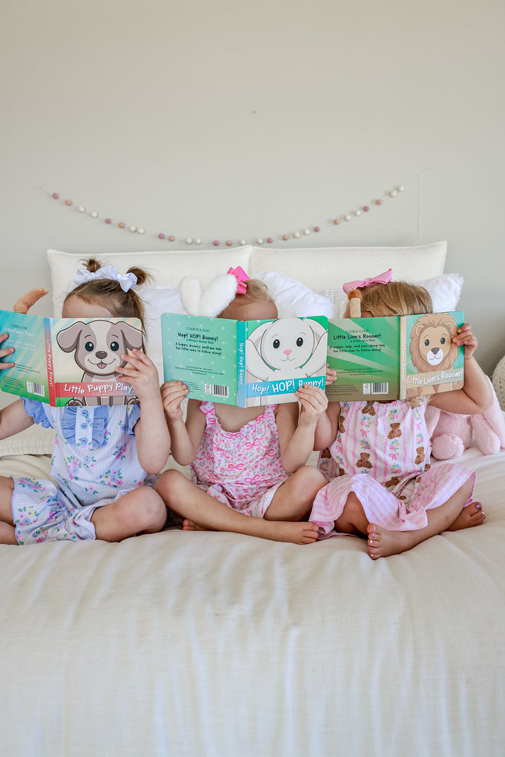 Three young girls on a bed reading Cuddle Plush Friends board books with plush animal tails