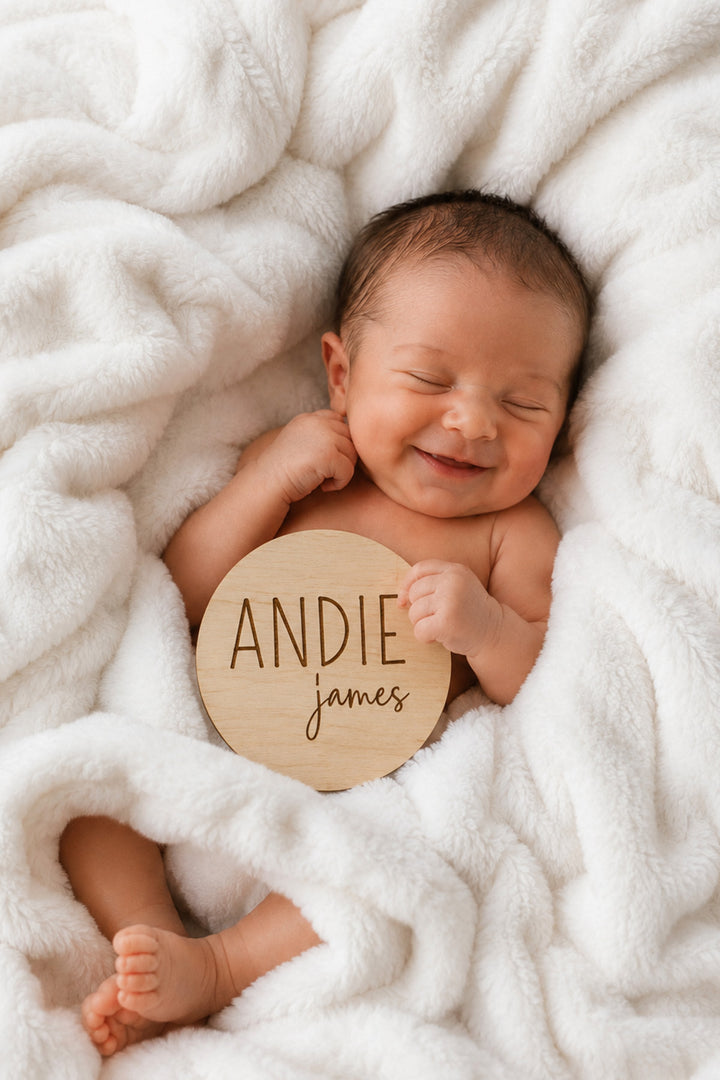 newborn wrapped in blanket holding wood name announcement block and script font