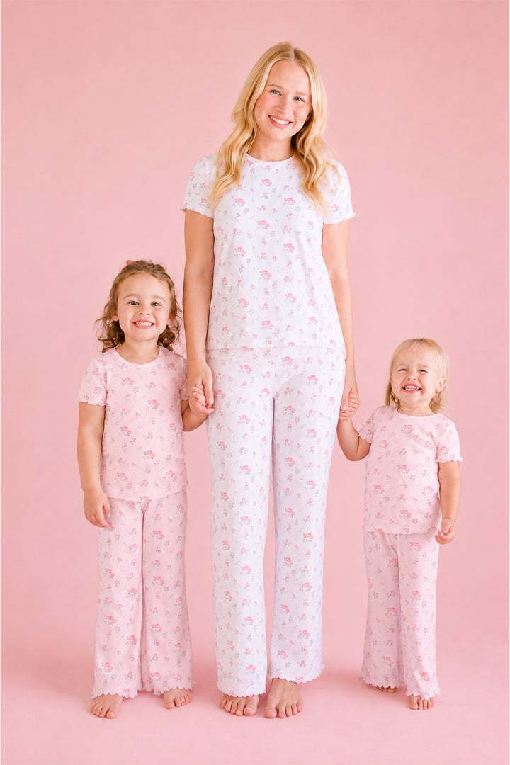 A woman and two young girls wearing Caden Lane matching pink and white short-sleeve pajama sets with a small floral print, standing together against a solid pink studio background.