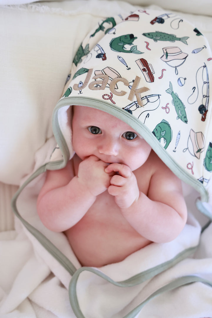 Baby wearing the Off The Hook embroidered bamboo hooded towel with custom embroidered name on the hood