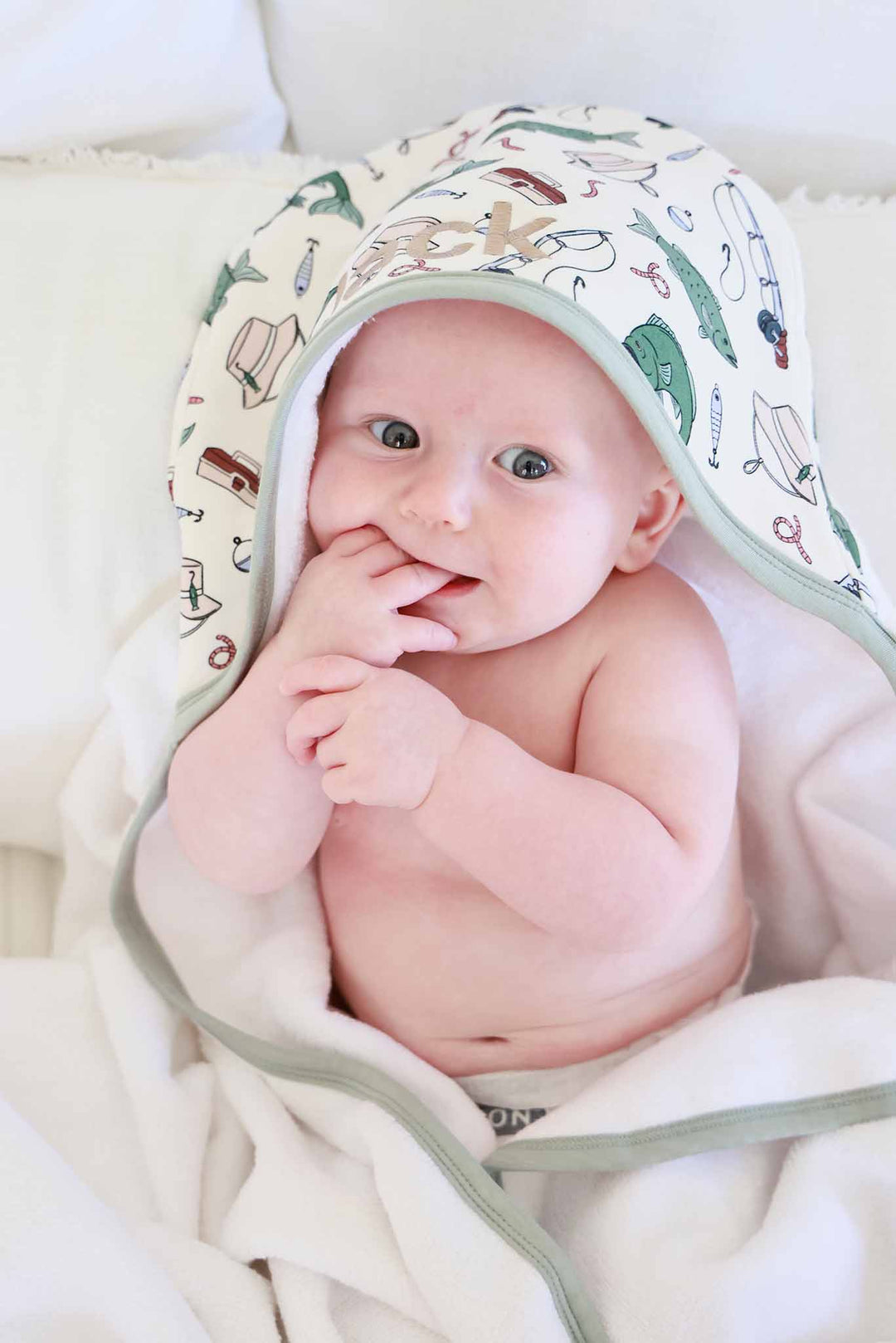 Close-up of baby wearing the Off The Hook bamboo hooded towel with sage green trim and fishing print