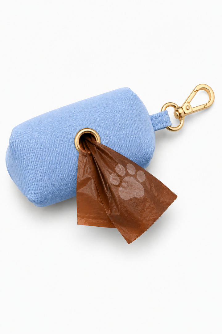 Caden Lane denim days light blue waste bag holder with paw print waste bag partially dispensed and gold carabiner clip