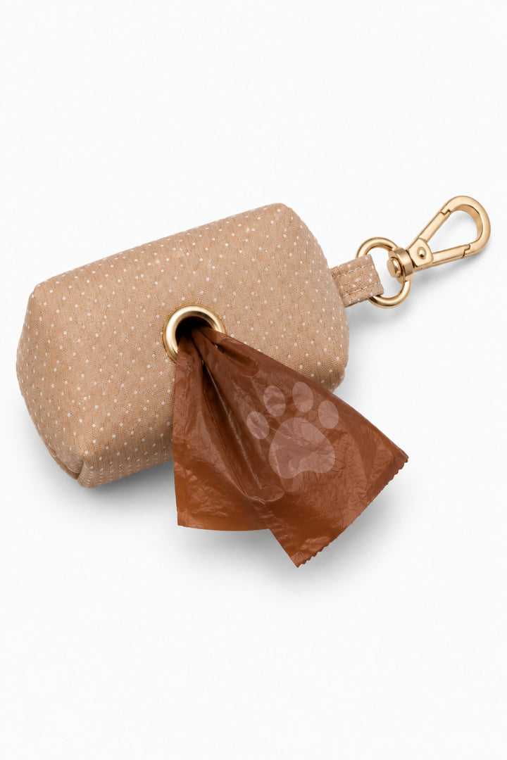 Latte brown polka dot pet waste bag holder with gold hardware and carabiner clip, with a brown paw print waste bag dispensing from the bottom