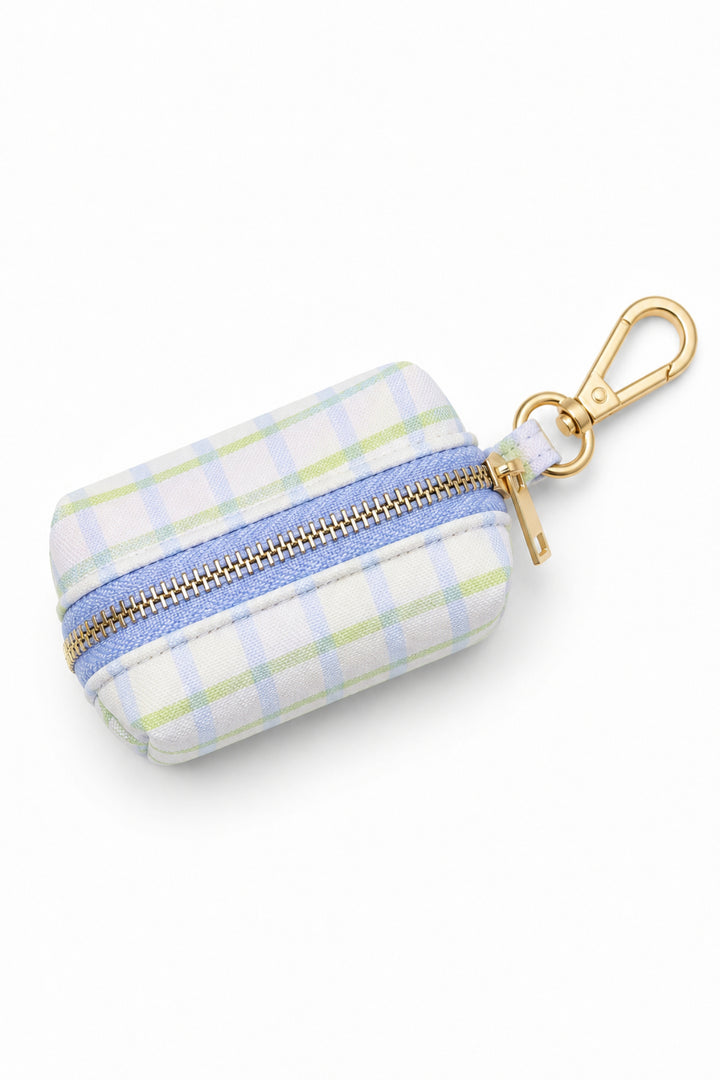 Pet waste bag holder in green and blue picnic plaid fabric with a gold zipper across the middle and a gold carabiner clip, shown from the top