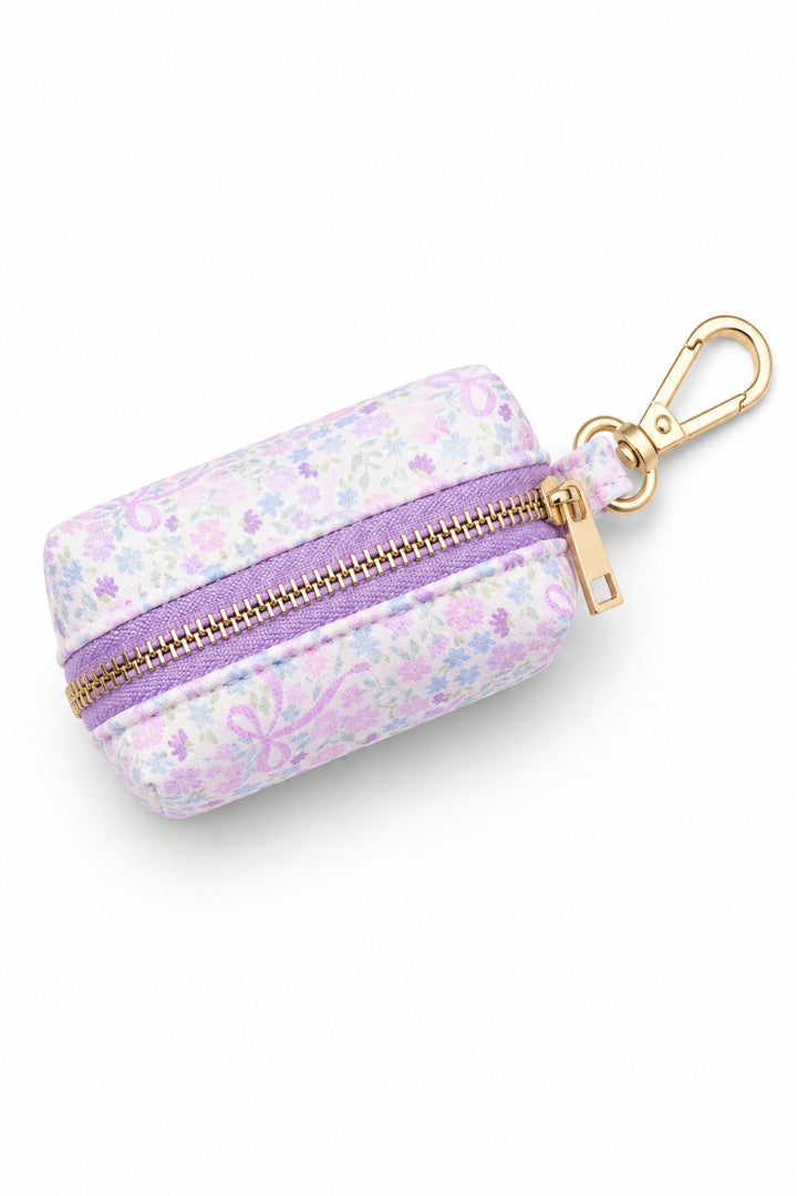 Pet waste bag holder in the Ribbon Garden print — pink and lavender floral fabric — with a purple zipper and gold carabiner clip, shown from the top on a white background