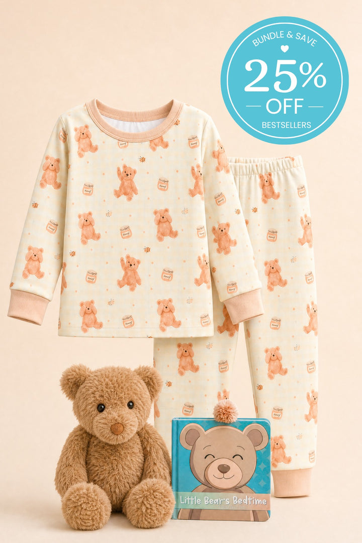 Flat lay of a Caden Lane cream two-piece pajama set in a honey bear print, paired with a plush teddy bear and a "Little Bear's Bedtime" board book.