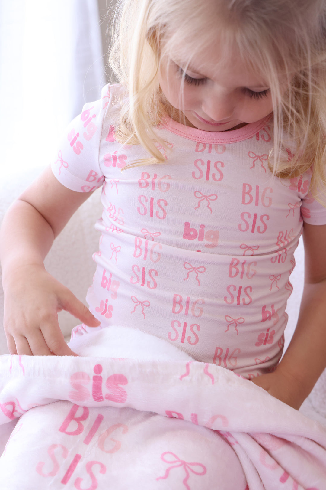 closeup of girl wearing big sis pajama set with the matching blanket across her lap 