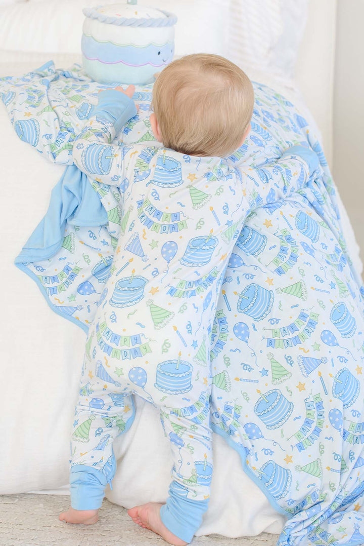 A baby wearing Caden Lane birthday pajamas, holding a matching birthday blanket. 