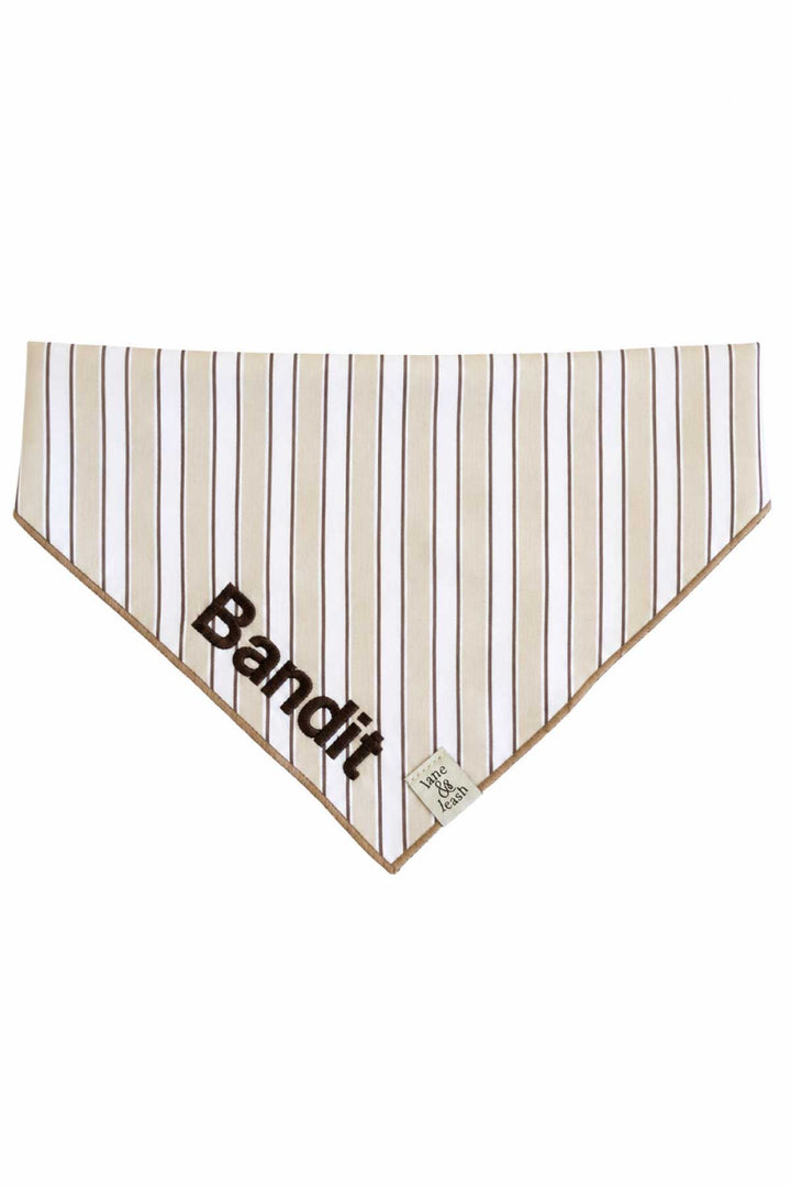 Flat-lay of embroidered pet bandana in Biscuit Stripe pattern with the name Bandit embroidered in bold letters across the front