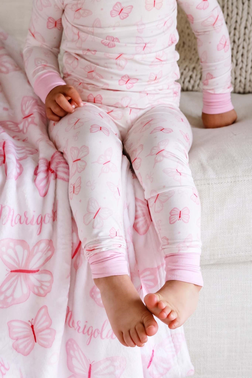 Two Piece Pajama Set in Blooming Butterflies print - close-up of toddler's legs and feet in the butterfly-print pajama pants sitting on a personalized blanket