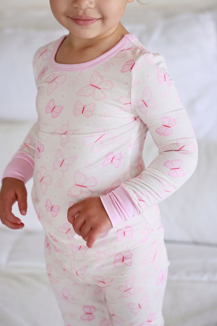 Two Piece Pajama Set in Blooming Butterflies print - front view of toddler standing wearing the full two-piece set with long-sleeve top and matching pants, pink trim on neckline and cuffs