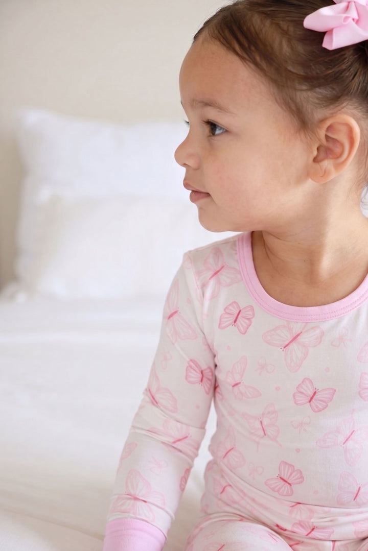 Two Piece Pajama Set in Blooming Butterflies print - close-up side profile of toddler wearing the butterfly print long-sleeve pajama top with pink bow headband