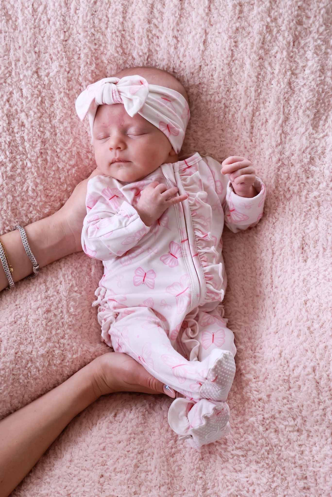Ruffle Zipper Footie in Blooming Butterflies print - full length view of newborn in the butterfly print footie holding a stuffed bunny, showing the complete footed one-piece design with ruffle trim