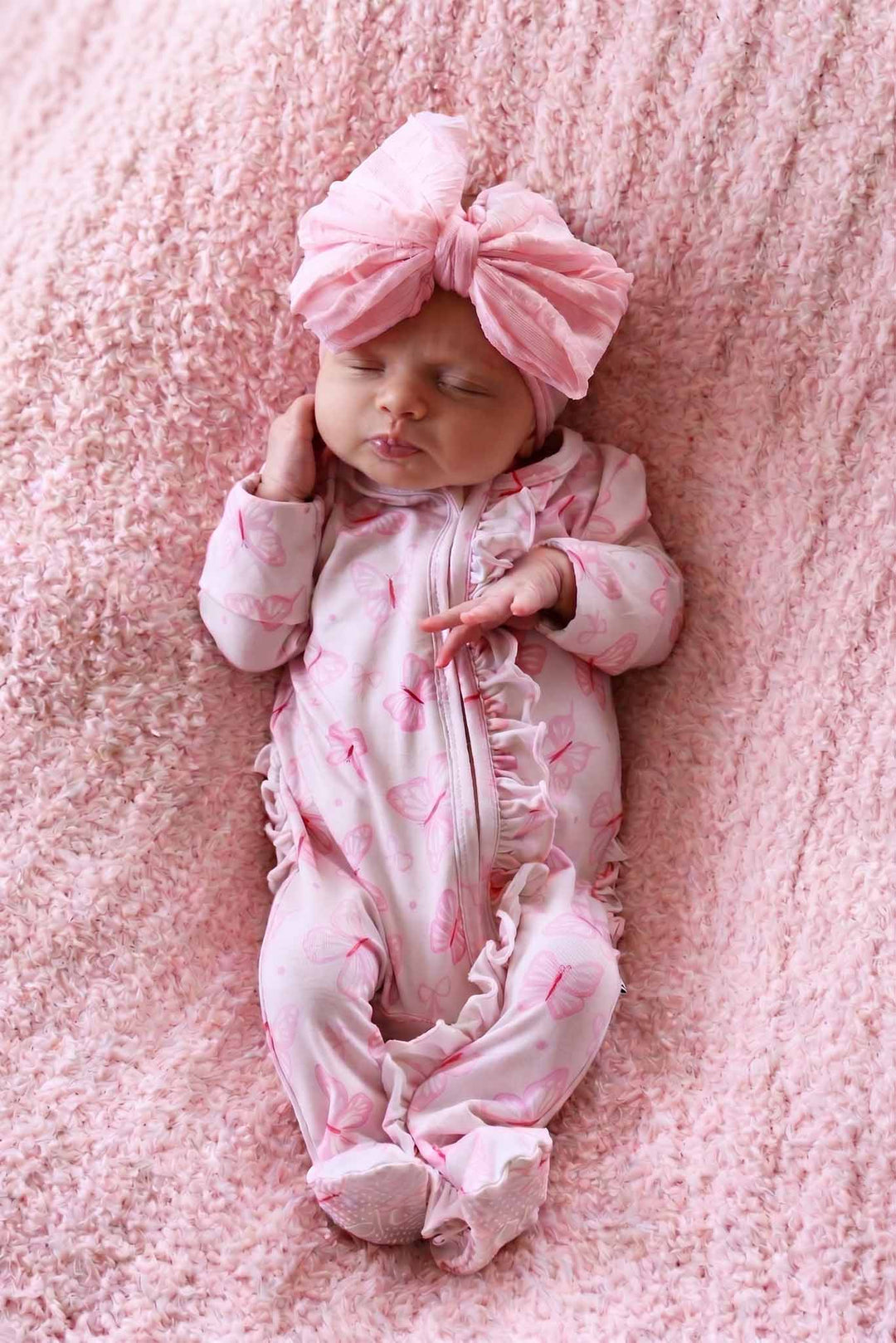 Ruffle Zipper Footie in Blooming Butterflies print - newborn baby in the butterfly print footie lying beside a stuffed bunny on pink satin, with the ruffle trim clearly visible