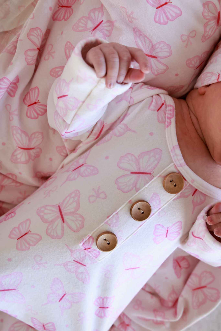 Newborn Baby Knot Gown & Hat Set in Blooming Butterflies print - close-up of baby in the gown highlighting the gold button snaps and detailed pink butterfly print fabric
