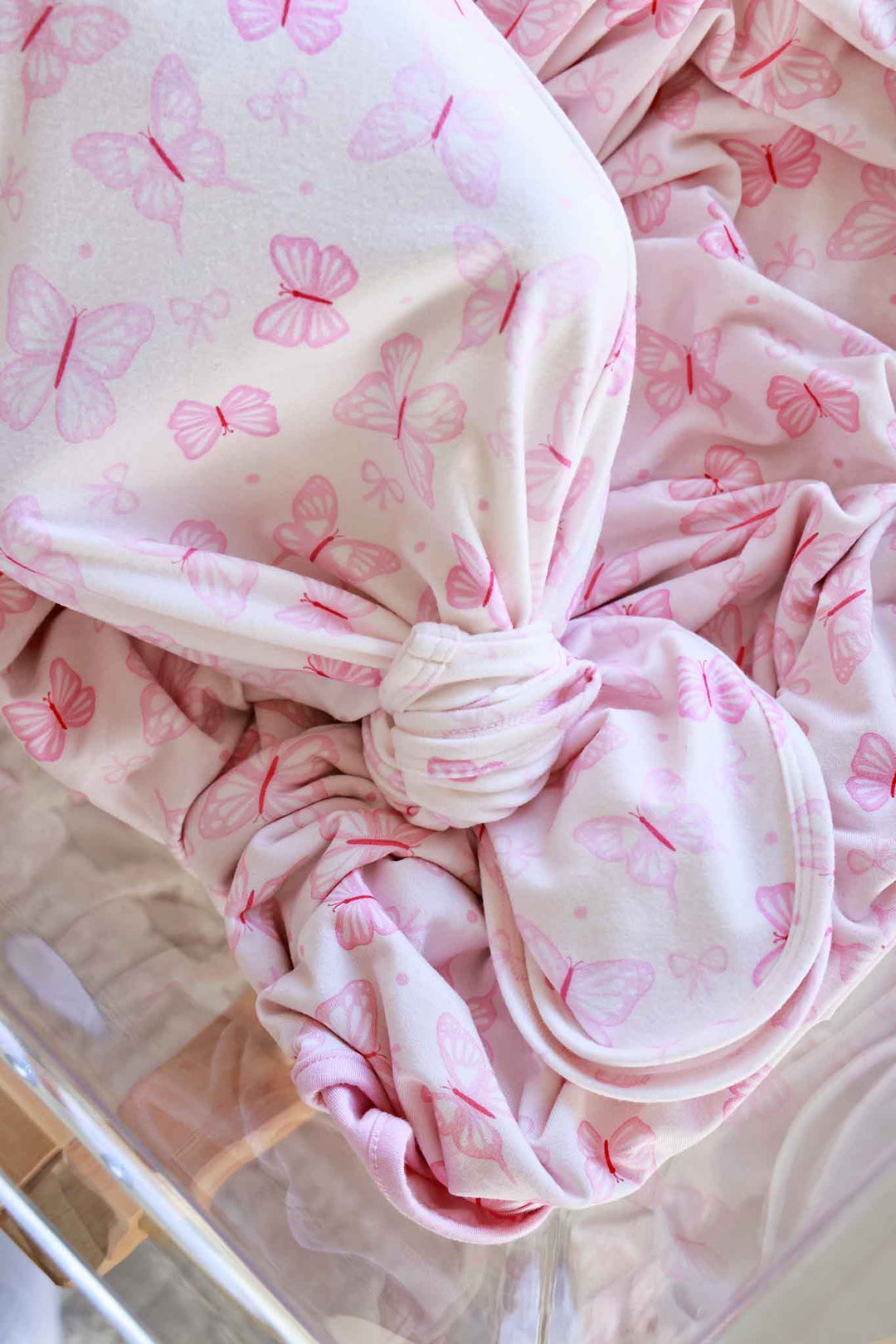 Newborn Baby Knot Gown & Hat Set in Blooming Butterflies print - close-up of newborn wearing the gown and matching hat in bassinet, with gold button snaps and butterfly print visible
