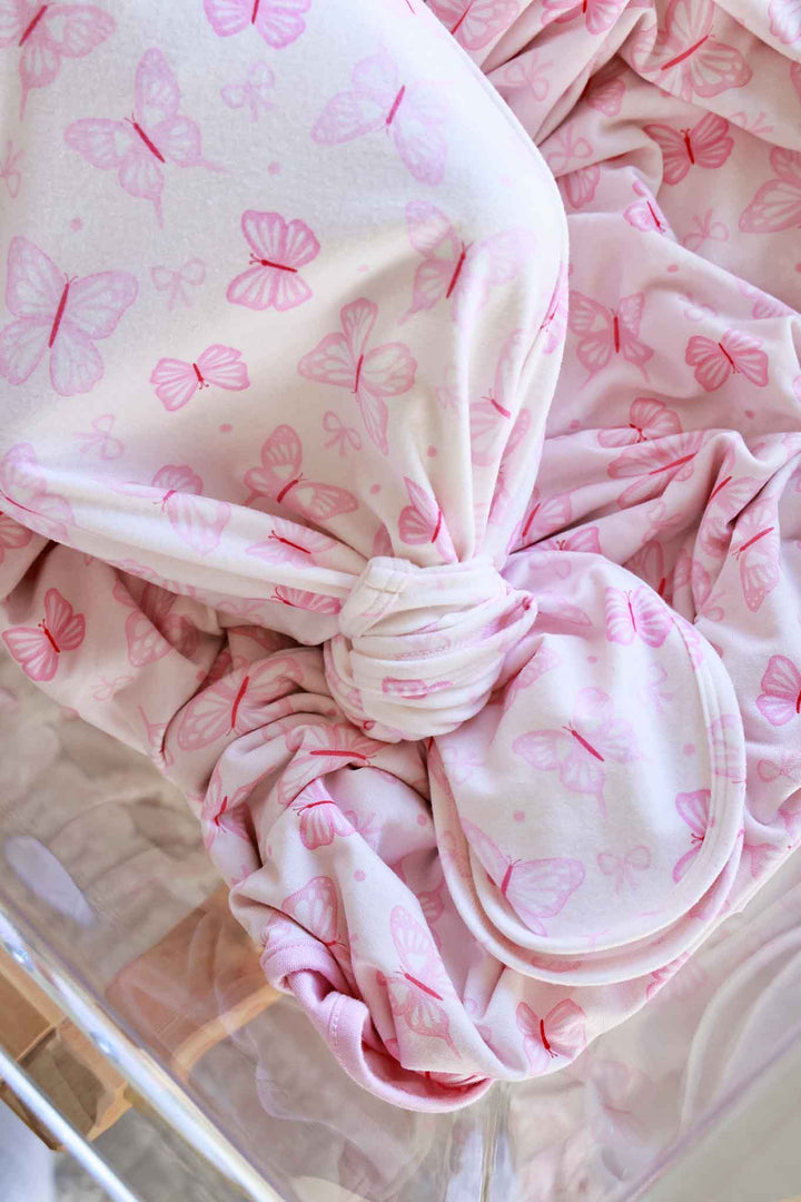 Newborn Baby Knot Gown & Hat Set in Blooming Butterflies print - close-up of newborn wearing the gown and matching hat in bassinet, with gold button snaps and butterfly print visible