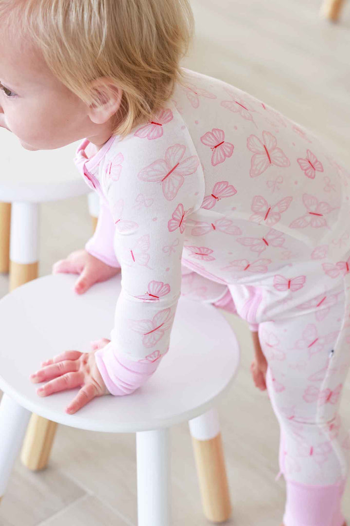 Convertible Zip Romper in Blooming Butterflies print - toddler leaning over a small stool wearing the full butterfly print zip romper, showing the back zipper and overall fit