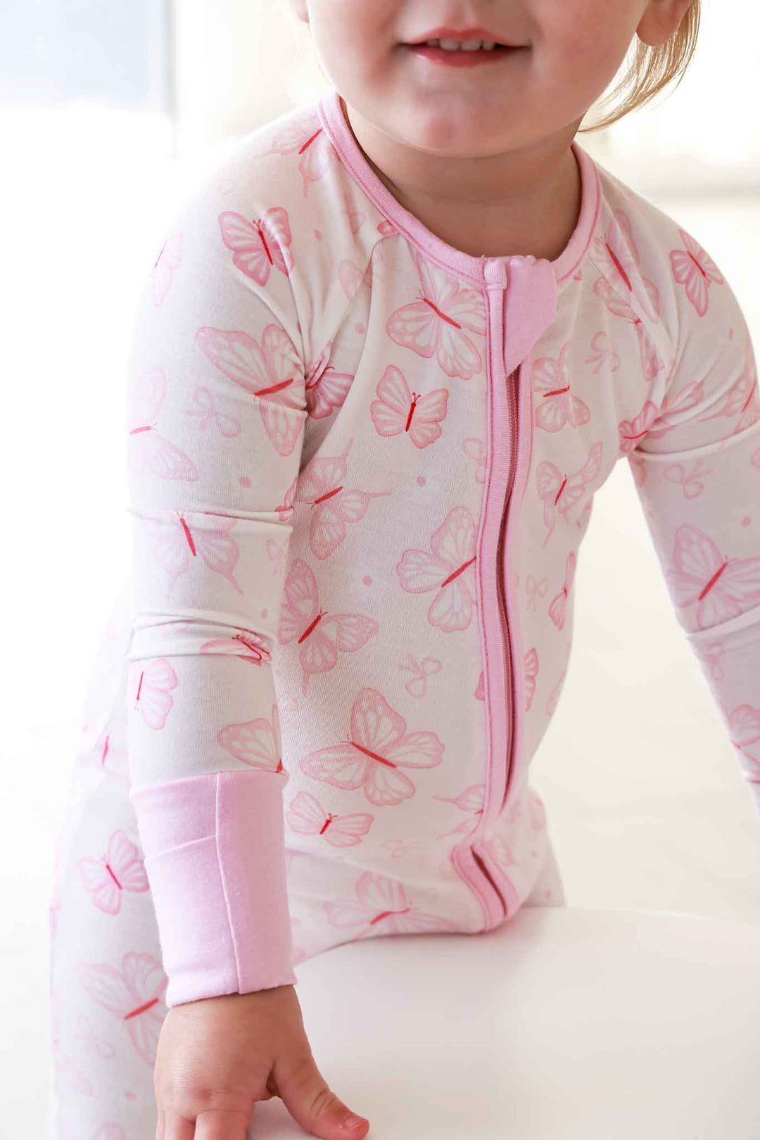 Convertible Zip Romper in Blooming Butterflies print - close-up of toddler wearing the romper, showing the front zipper detail and pink cuffed wrists with butterfly print fabric