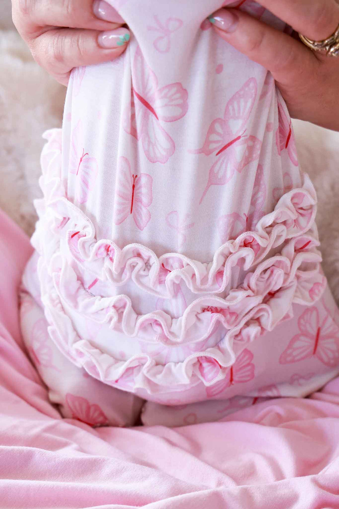 Ruffle Zipper Footie in Blooming Butterflies print - close-up of ruffle waist trim held by hands, showing the layered white ruffle detail against the pink butterfly print fabric