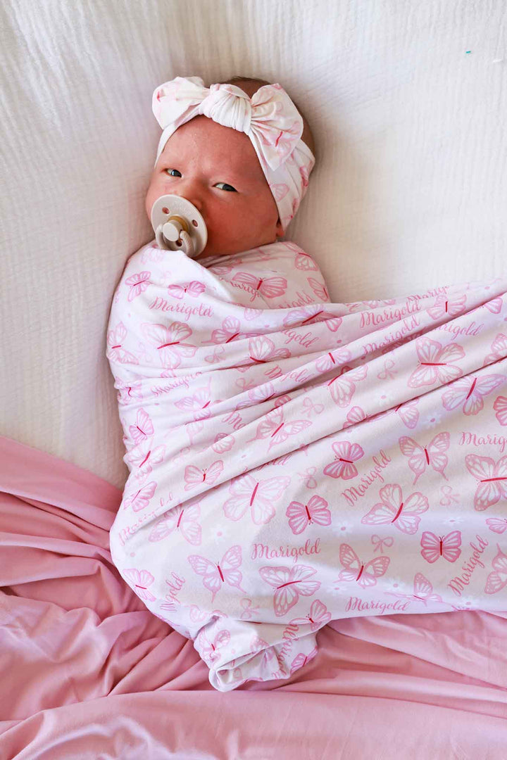 Personalized Swaddle Blanket in Blooming Butterflies print - newborn baby swaddled in the pink butterfly-print blanket with personalized name, wearing a matching headband