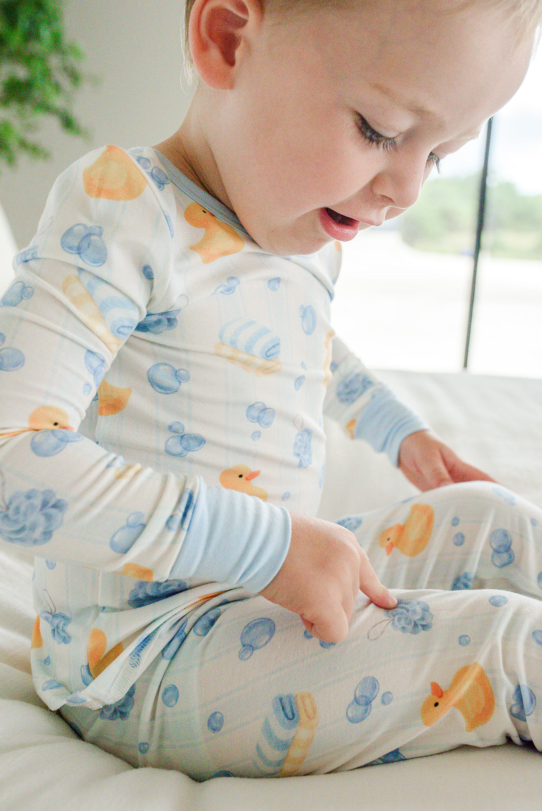 Baby boy sitting and looking down wearing blue Bubble Duckies two-piece bamboo pajamas showing duck print