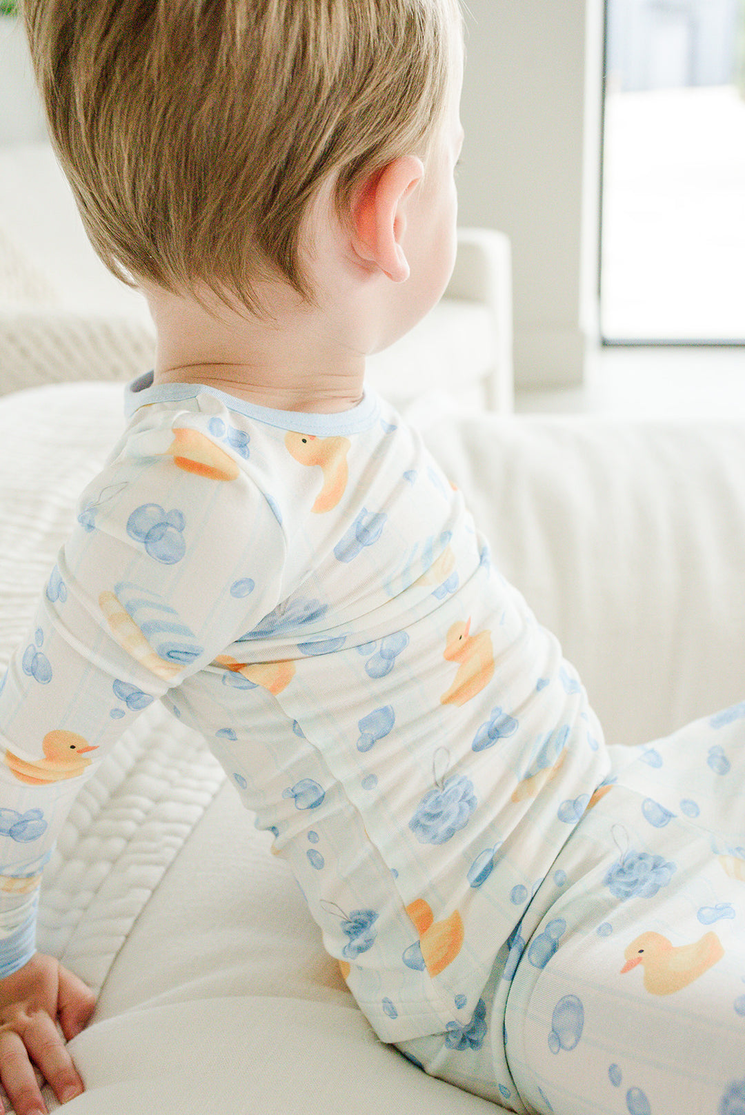 Back view of baby boy wearing blue Bubble Duckies two-piece bamboo pajama top with rubber duck print