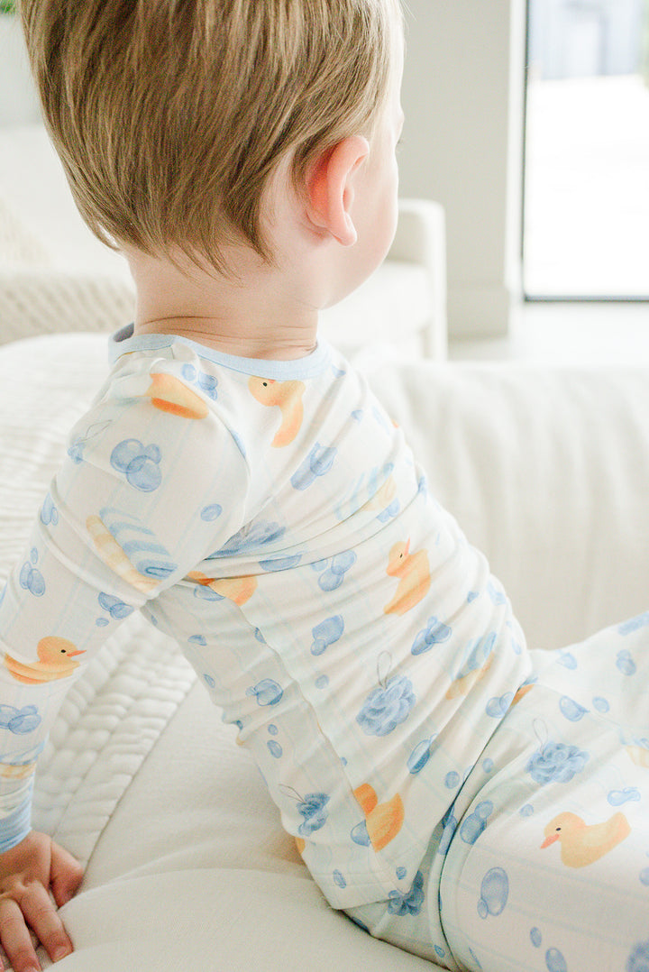 Back view of baby boy wearing blue Bubble Duckies two-piece bamboo pajama top with rubber duck print