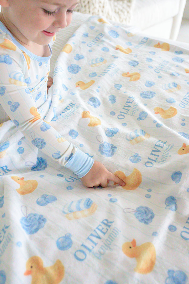 Boy looking down while holding blue Bubble Duckies personalized blanket with yellow rubber duck print