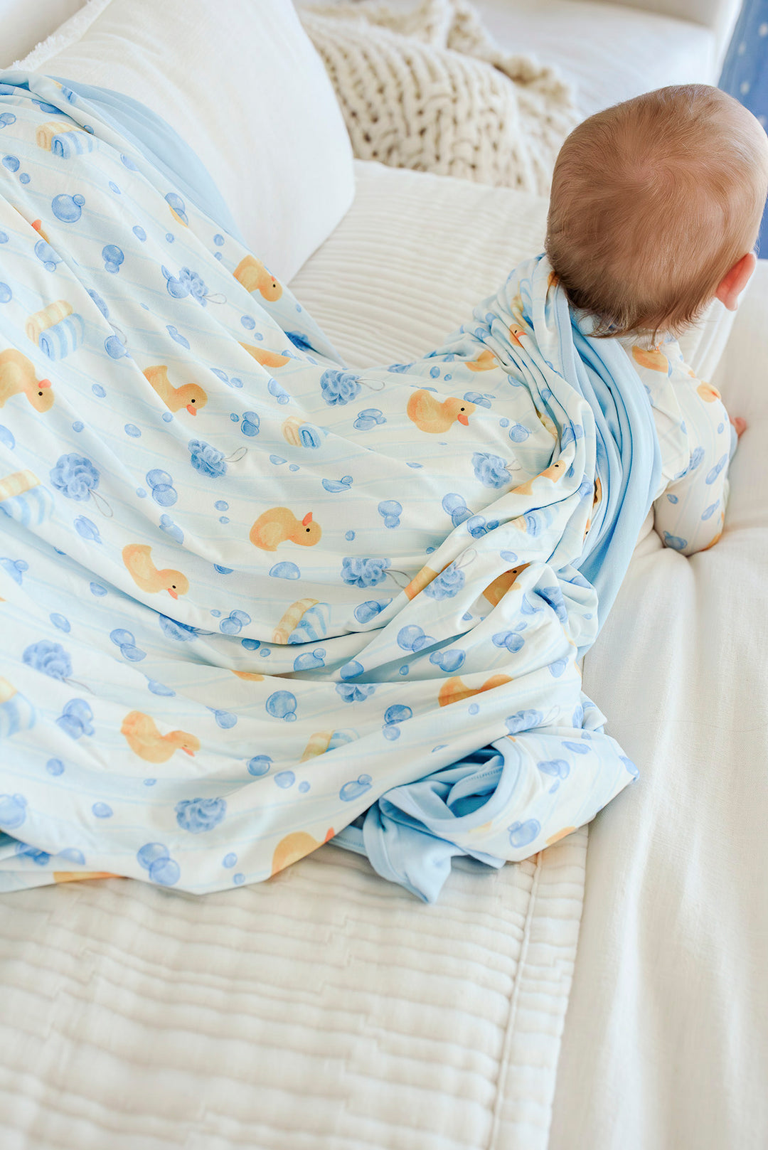 Baby lying on blue Bubble Duckies double-sided bamboo blanket showing printed duck side and solid blue reverse