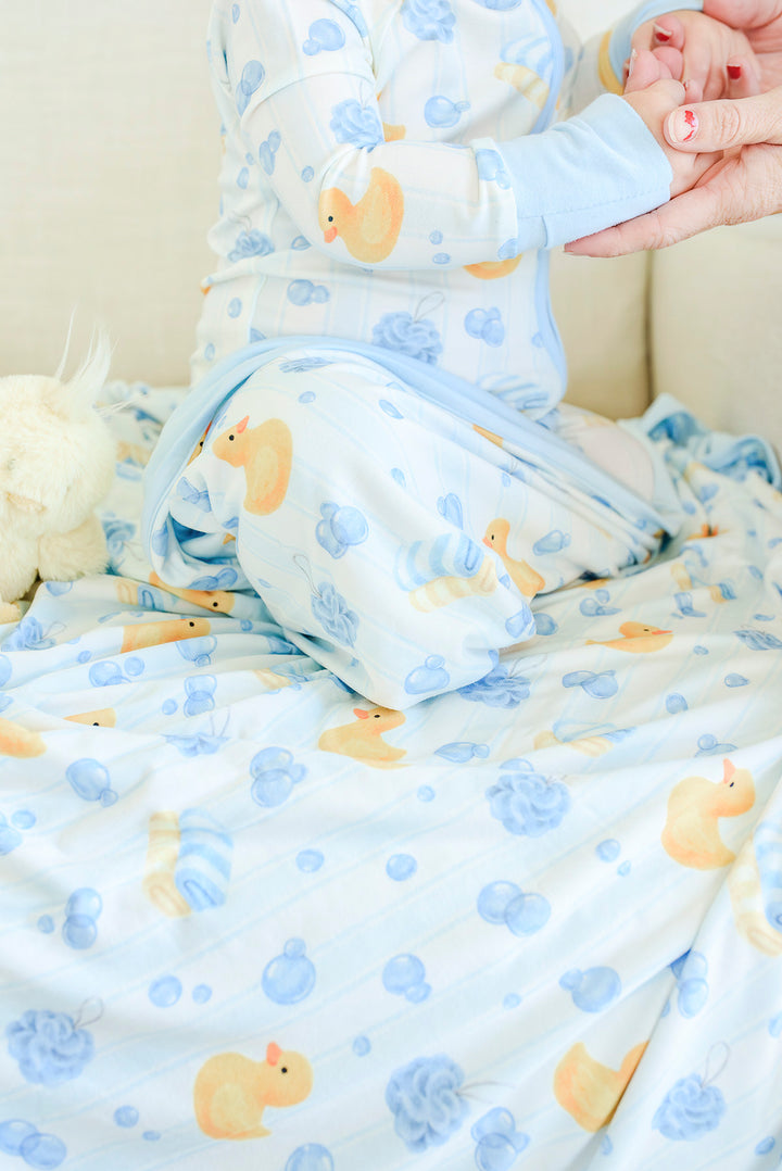 Adult holding baby wrapped in blue Bubble Duckies bamboo blanket with yellow rubber duck and blue bubble print