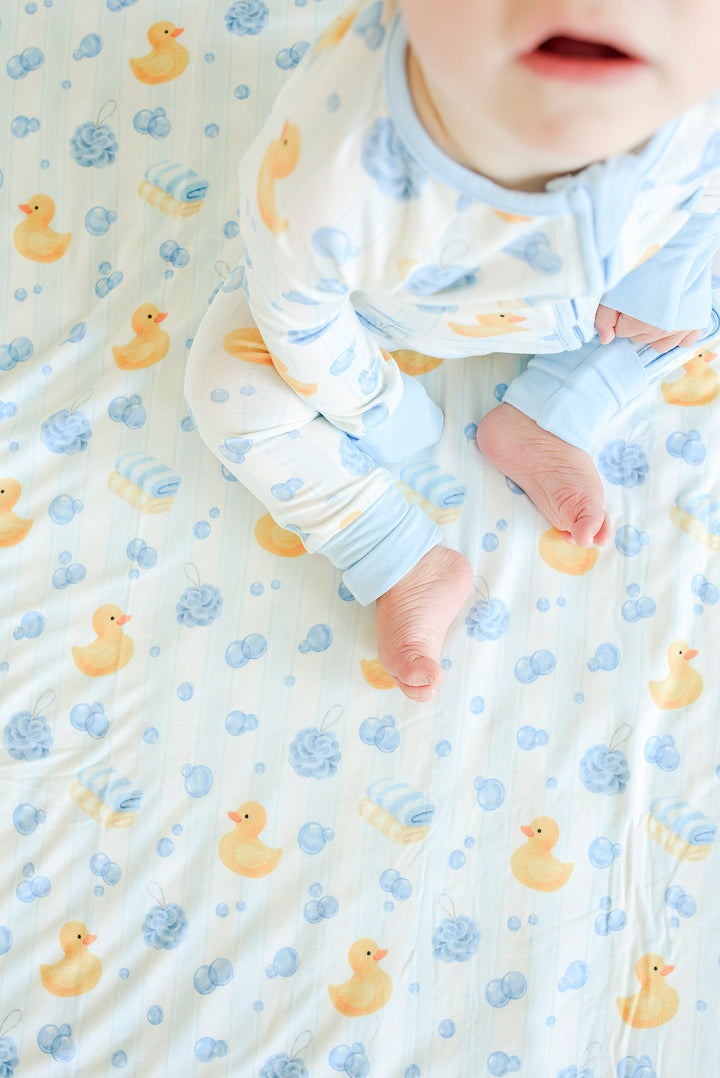 Overhead view of baby lying on blue Bubble Duckies bamboo blanket with yellow rubber duck print