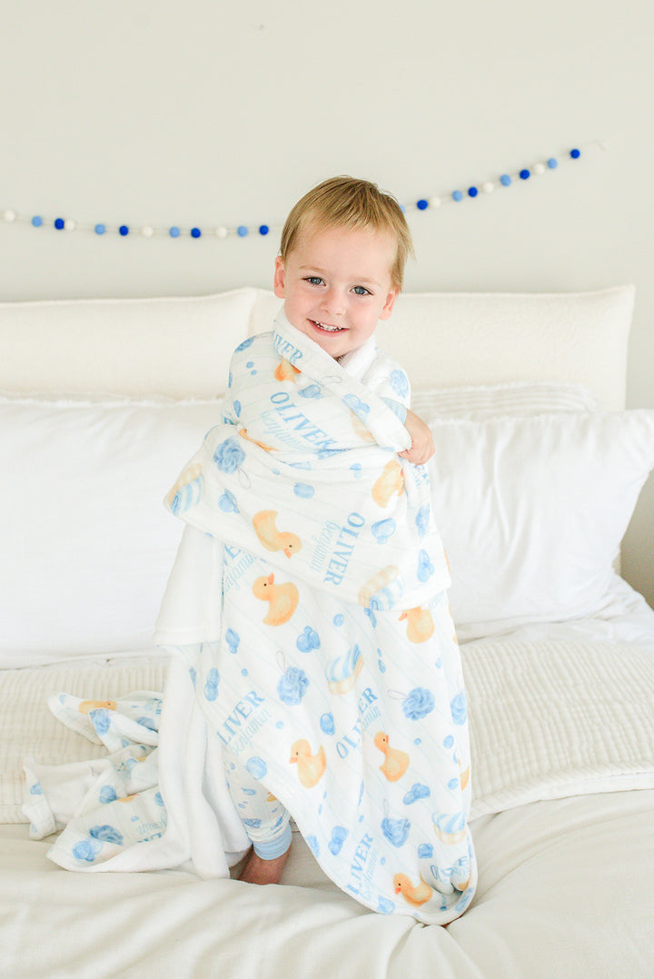 Baby boy smiling and wrapped in blue Bubble Duckies personalized blanket with rubber duck and bubble print