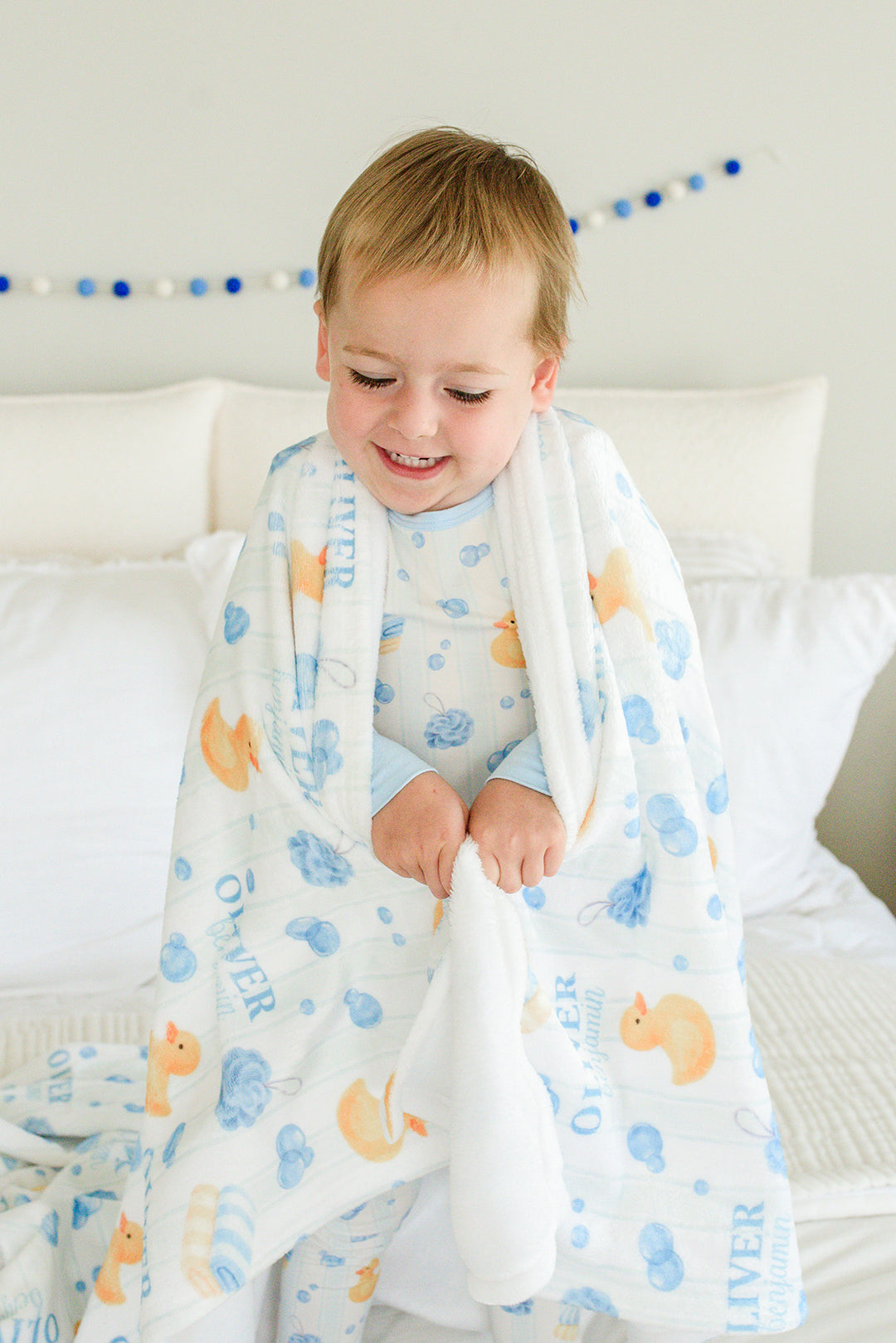 Toddler boy with blue Bubble Duckies personalized kids blanket showing duck and bubble print with custom name