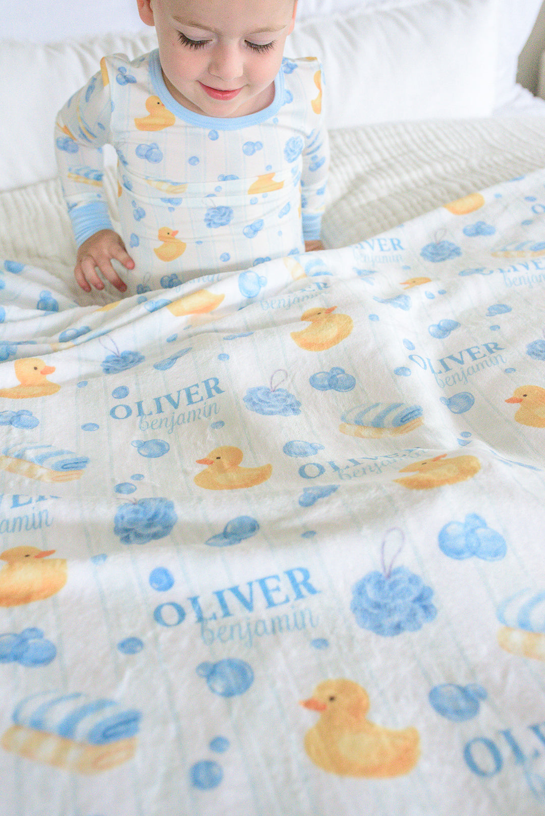Toddler boy wrapped in blue Bubble Duckies personalized blanket looking sideways with custom name print