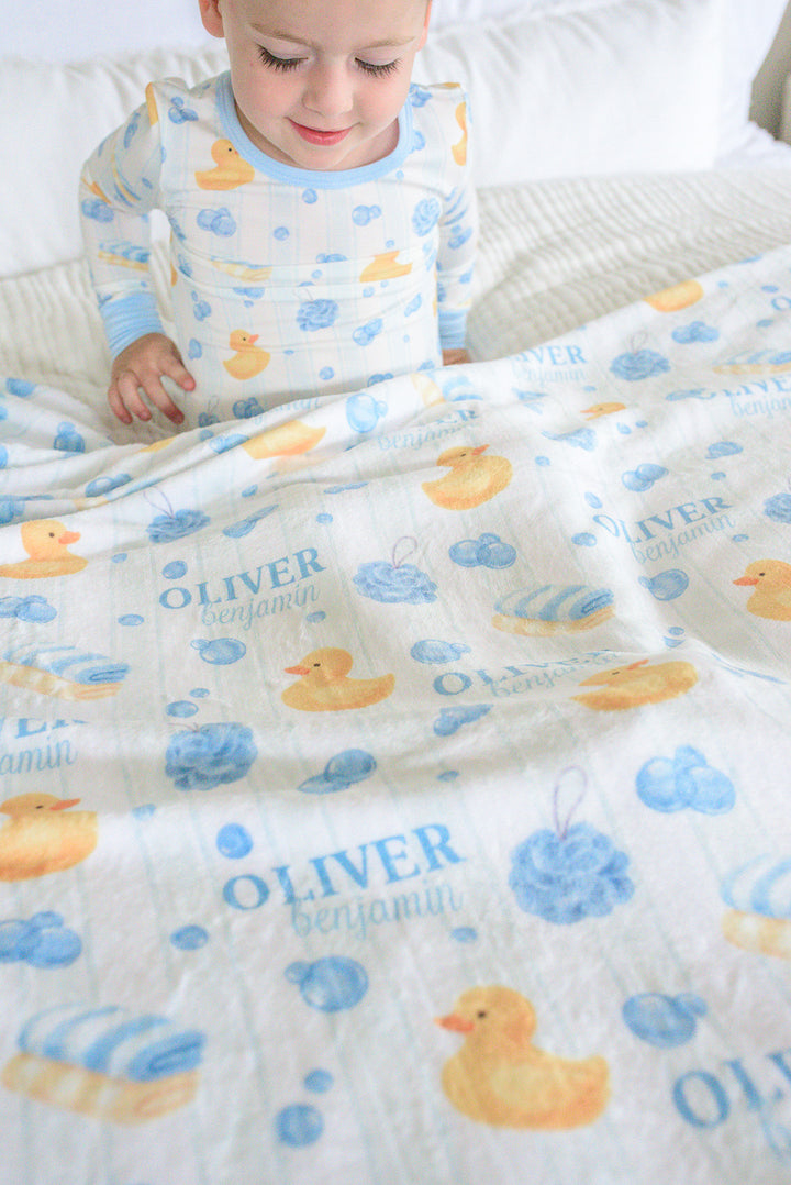 Toddler boy wrapped in blue Bubble Duckies personalized blanket looking sideways with custom name print