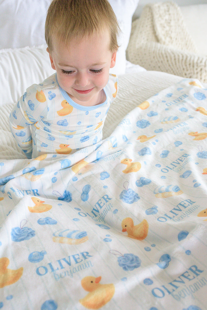 Smiling boy holding blue Bubble Duckies personalized kids blanket with yellow rubber duck and blue bubble print