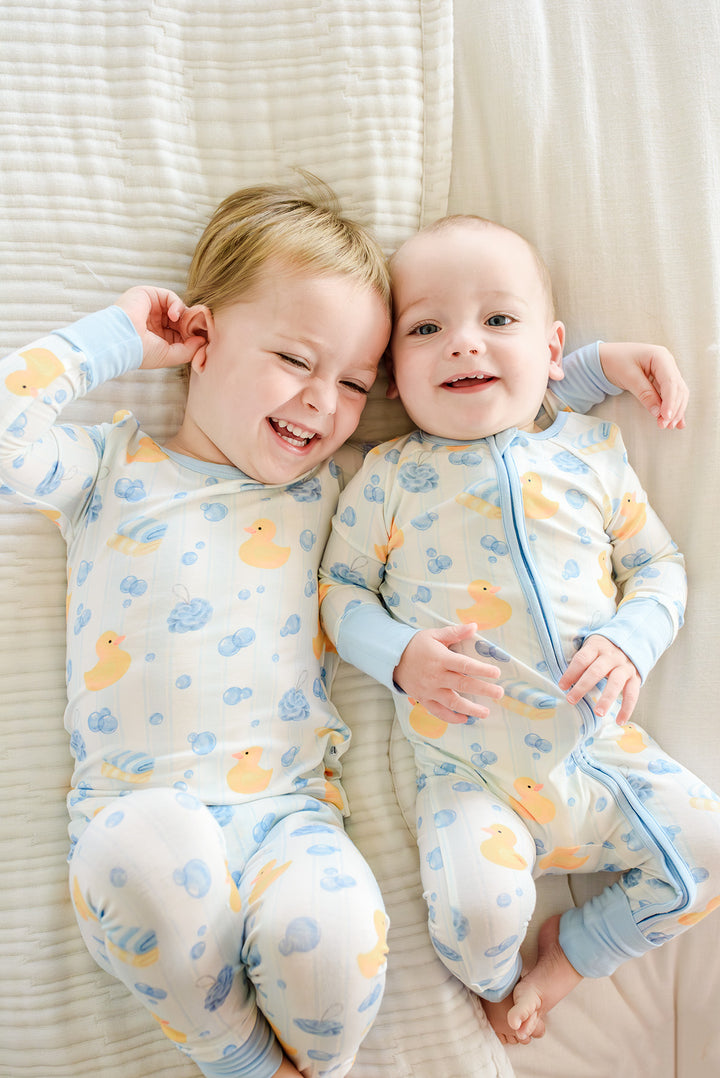 Two brothers lying together laughing in matching blue Bubble Duckies bamboo pajamas with yellow rubber duck print