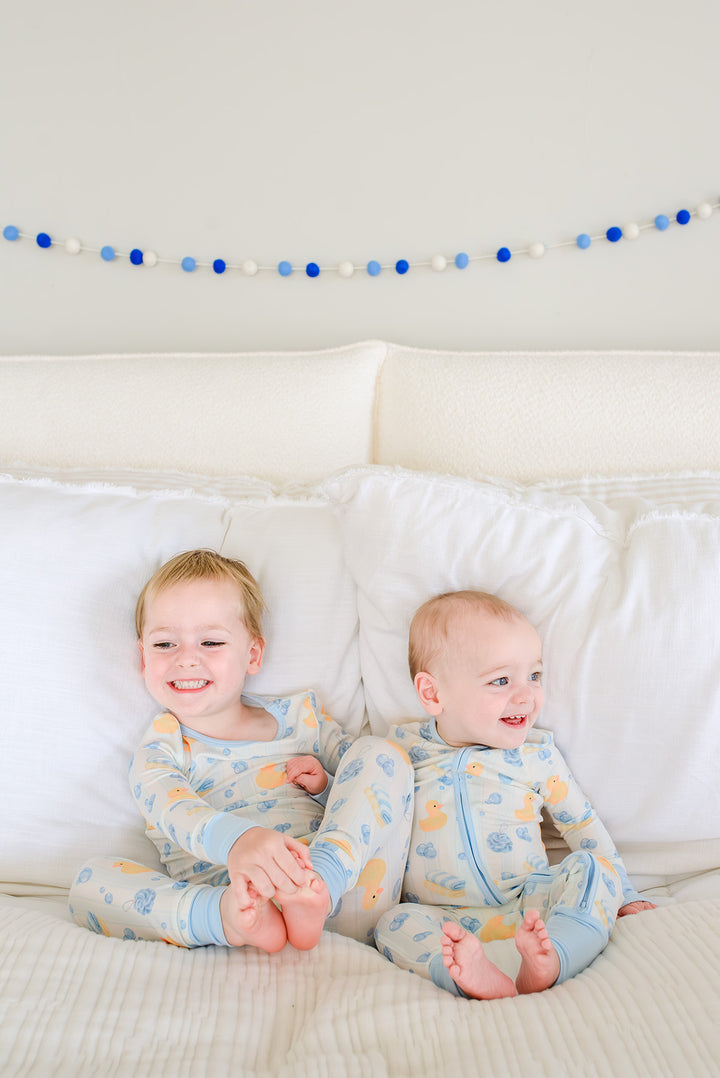 Close-up of two babies wearing blue and pink Bubble Duckies zip romper pajamas side by side with rubber duck print