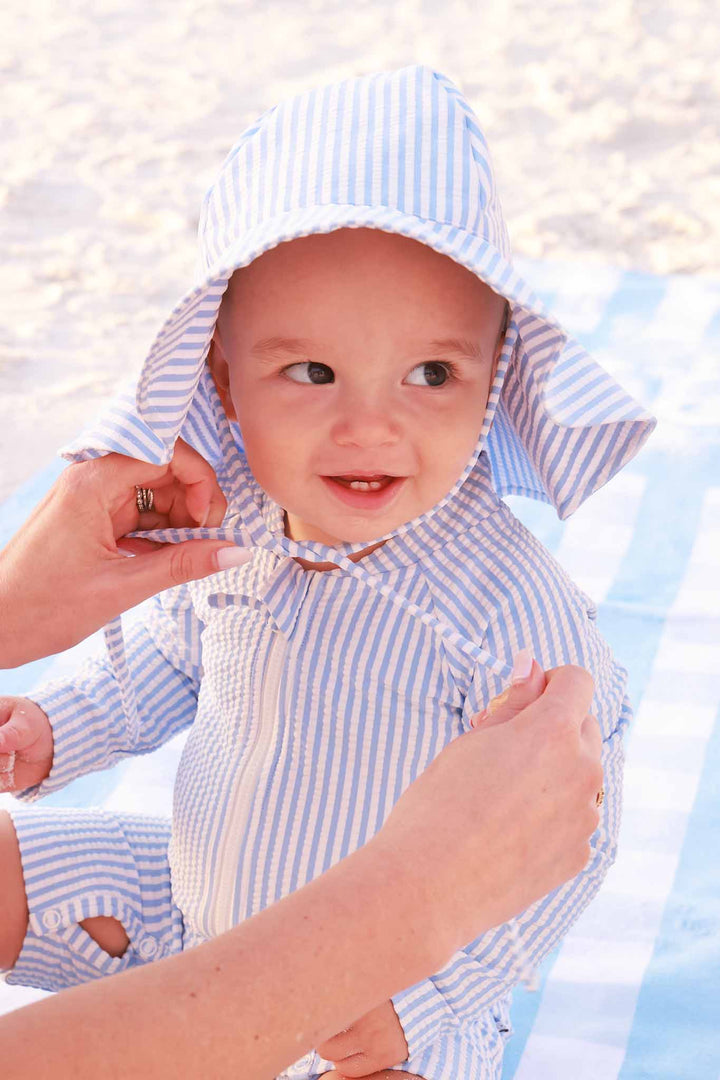 mom tying baby's hat wearing a matching blue seersucker swimsuit
