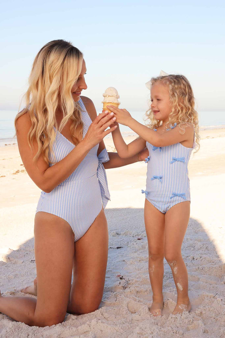 mom and daughter on beach holding an ice cream cone wearing matching blue seersucker swimsuits