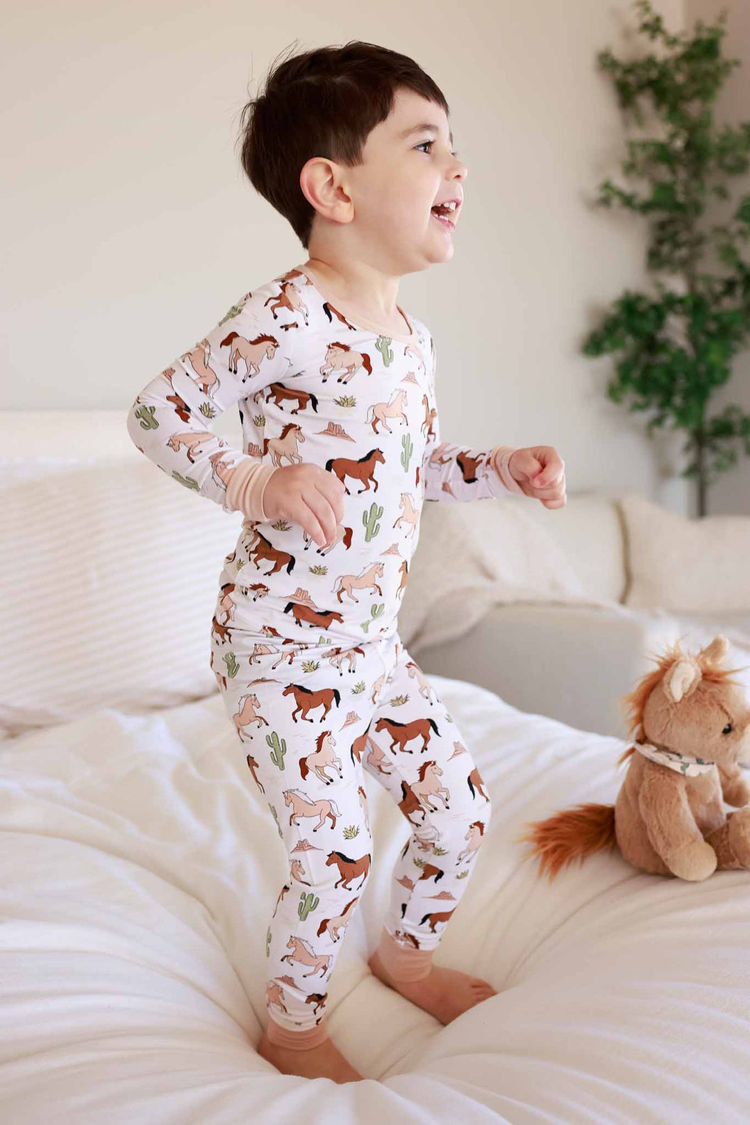 boy jumping on a bed in pony club neutral two piece pajama set 