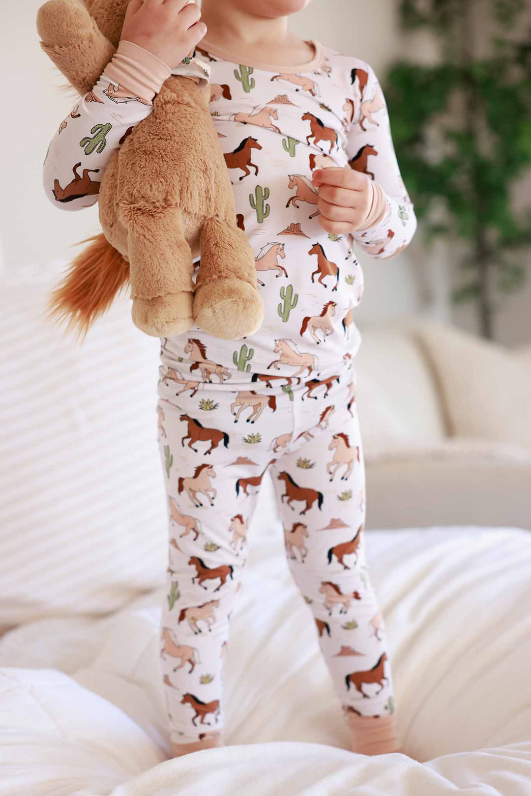 standing boy in pony club two piece pajama set holding stuffed horse 