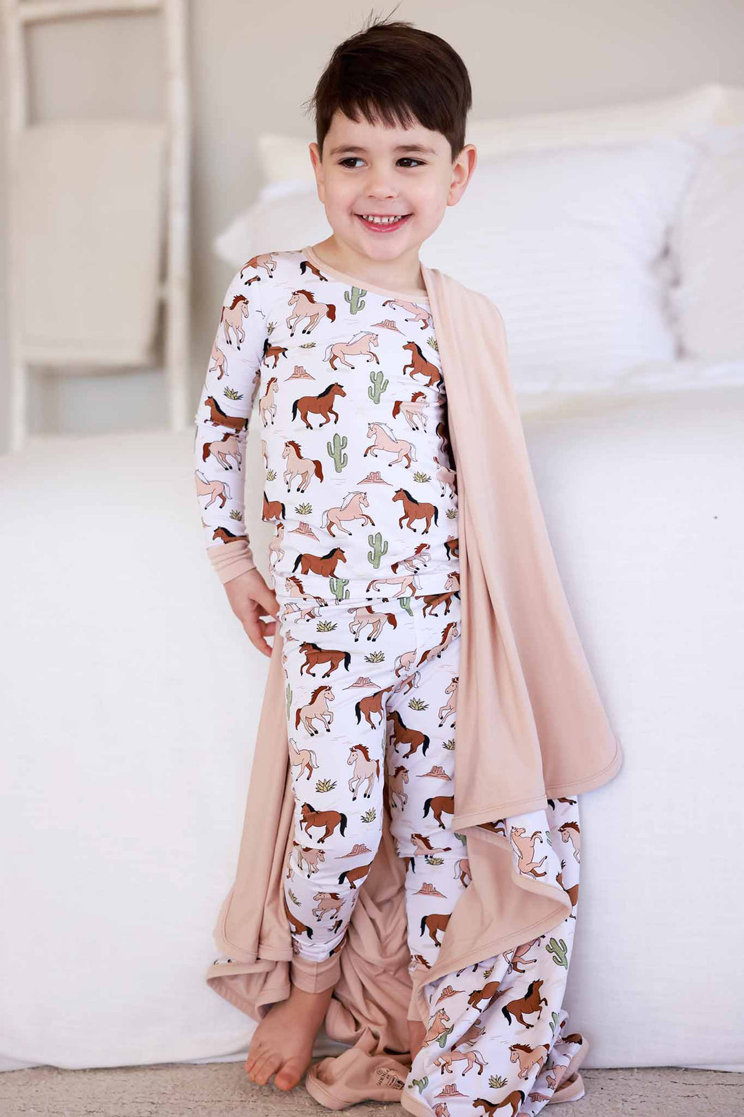 boy wearing neutral pony club double sided bamboo pajama set with a matching blanket draped over his shoulder