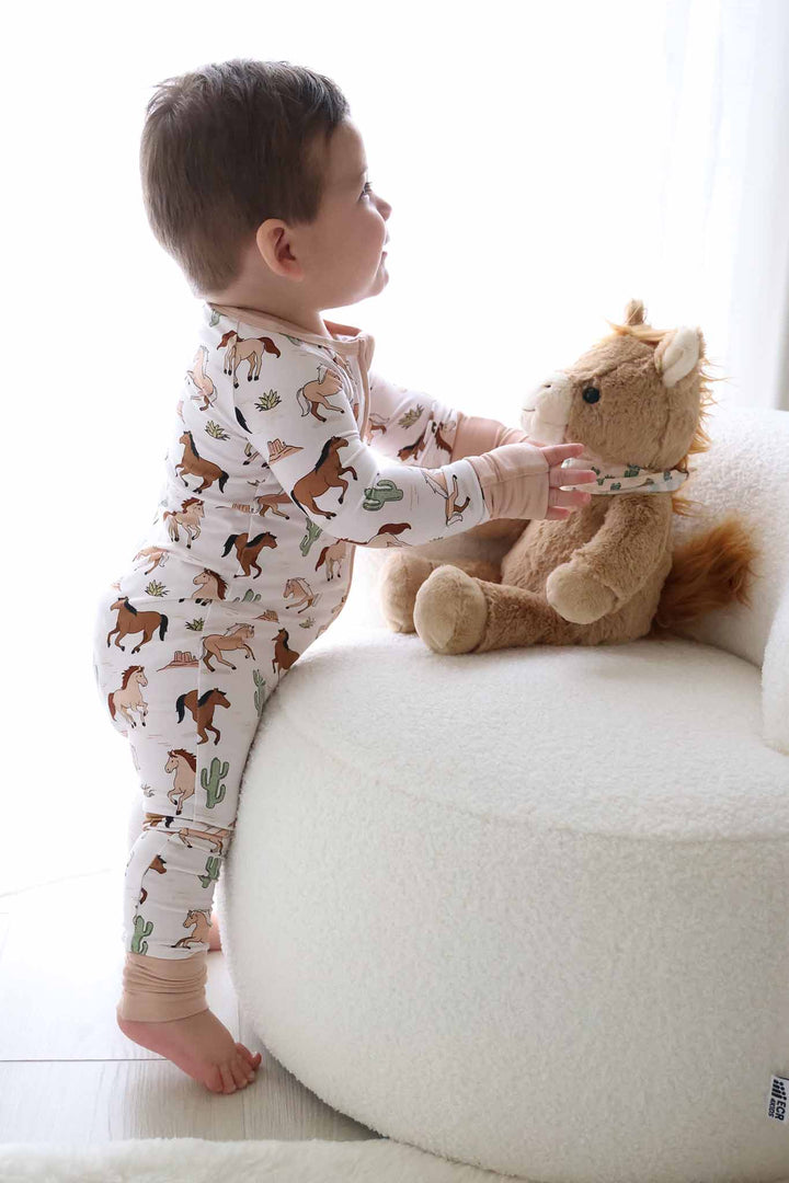 standing baby boy against white chair with stuffed horse 