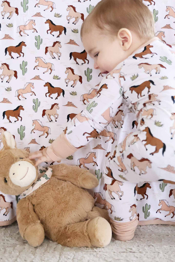 baby boy in horse zip romper bending down to touch stuffed horse 